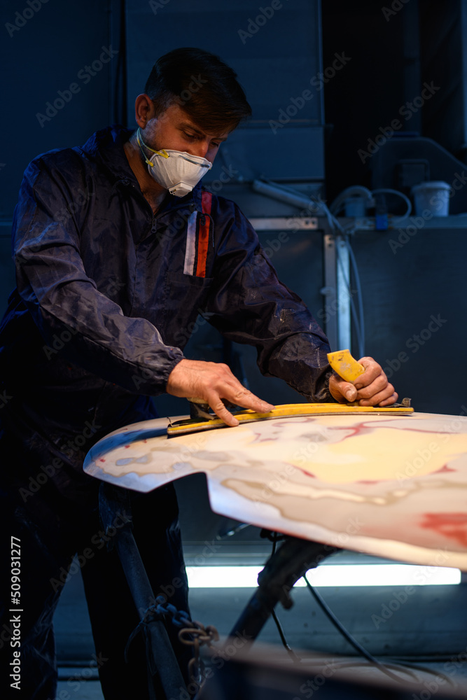 Workman in respirator grinding car bumper with sandpaper in garage Stock Photo Adobe Stock