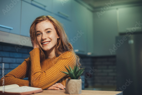 Caucasian redheaded woman with happy facial expression looking at camera with joy while reading a book. Front view portrait. Beautiful young girl. Beauty face