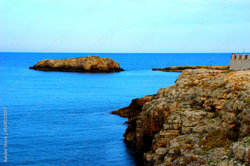 Fantastic scenery with a high massive coast of Polignano a Mare and a rocky island washed by the calm Adriatic sea reflecting the azure sky during the golden hour Fantastic scenery with a high massive coast of Polignano a Mare and a rocky island washed by the calm Adriatic sea reflecting the azure sky during the golden hour