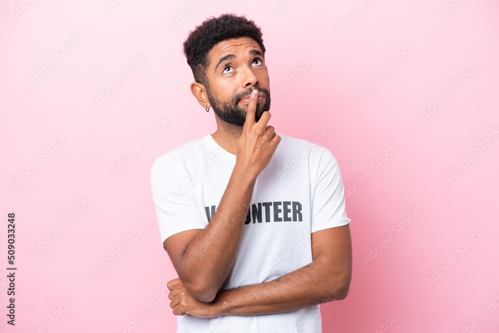 Young volunteer man isolated on pink background having doubts while looking up Young volunteer man isolated on pink background having doubts while looking up