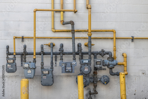 Natural gas distribution with meters, pipes and manifolds mounted on a cinder block exterior wall of a multi-unit commercial building, daytime, nobody