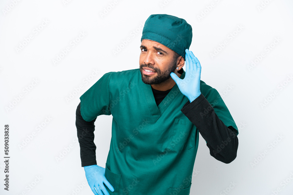 Surgeon Brazilian man in green uniform isolated on white background listening to something by putting hand on the ear Surgeon Brazilian man in green uniform isolated on white background listening to something by putting hand on the ear