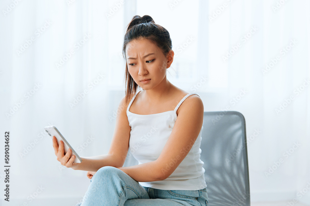 Wary irritated angry tanned lovely young Asian woman read bad news at call using phone at home interior living room. Distance communication Social media concept. Cool offer Banner Wide angle Wary irritated angry tanned lovely young Asian woman read bad news at call using phone at home interior living room. Distance communication Social media concept. Cool offer Banner Wide angle