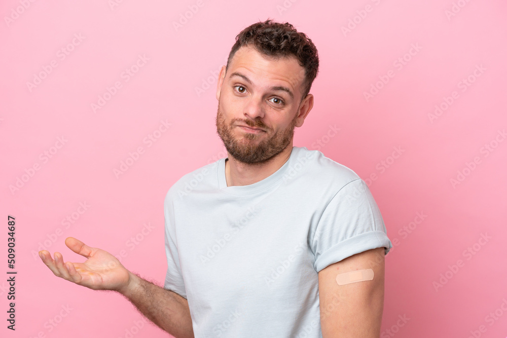 Young Brazilian man wearing a band-aids isolated on pink background making doubts gesture while lifting the shoulders Young Brazilian man wearing a band-aids isolated on pink background making doubts gesture while lifting the shoulders