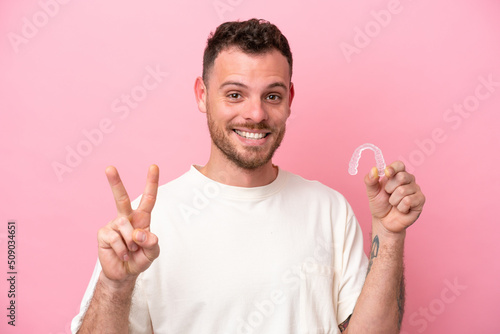 Brazilian man holding invisible braces smiling and showing victory sign