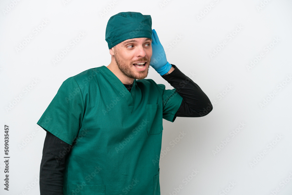 Surgeon Brazilian man in green uniform isolated on white background listening to something by putting hand on the ear Surgeon Brazilian man in green uniform isolated on white background listening to something by putting hand on the ear