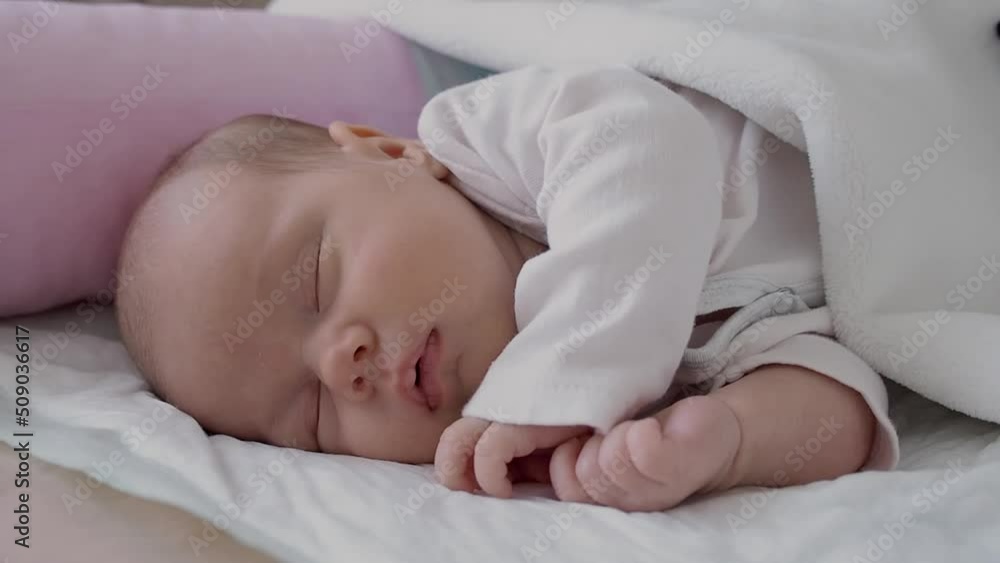 cute little newborn baby girl peacefully sleeps in the nursery on a white cotton bed. selective focus cute little newborn baby girl peacefully sleeps in the nursery on a white cotton bed. selective focus