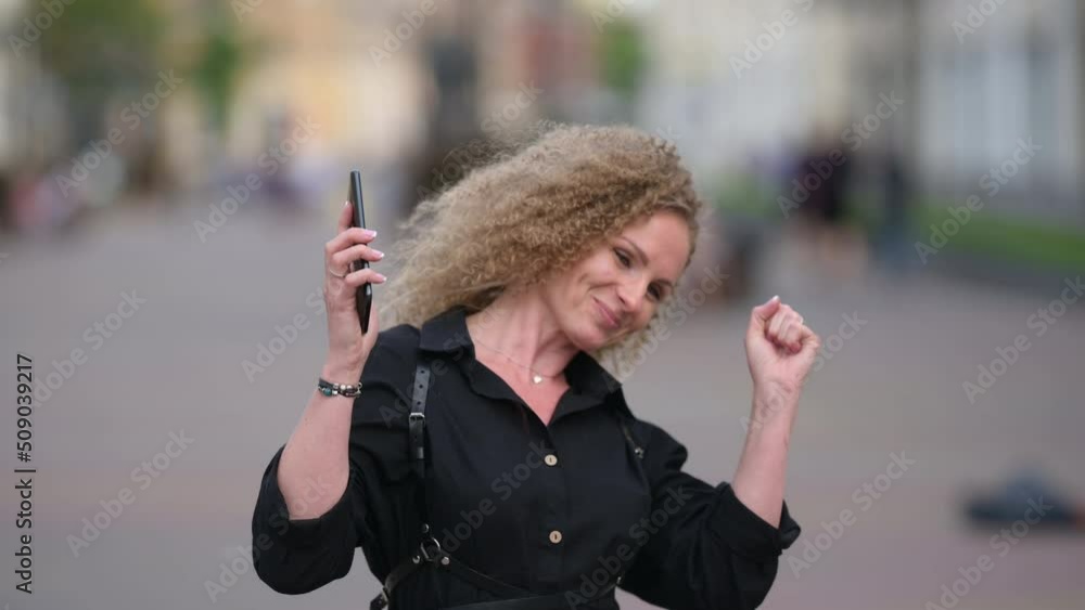Portrait of a young attractive Woman on a City Street Using her phone looks and sees the message with a good news. Female using mobile cell phone just found out great big win Portrait of a young attractive Woman on a City Street Using her phone looks and sees the message with a good news. Female using mobile cell phone just found out great big win
