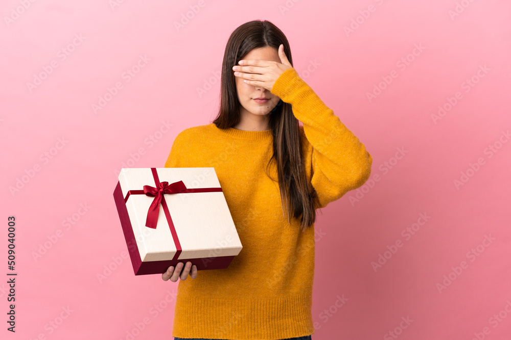 Teenager Brazilian girl holding a gift over isolated pink background covering eyes by hands. Do not want to see something Teenager Brazilian girl holding a gift over isolated pink background covering eyes by hands. Do not want to see something