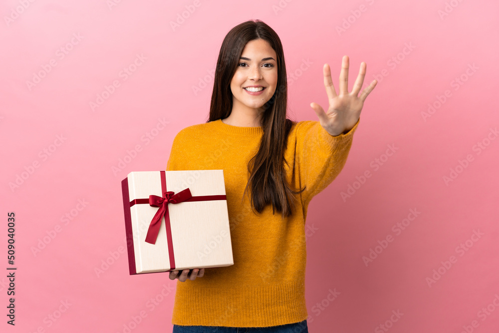 Teenager Brazilian girl holding a gift over isolated pink background counting five with fingers Teenager Brazilian girl holding a gift over isolated pink background counting five with fingers