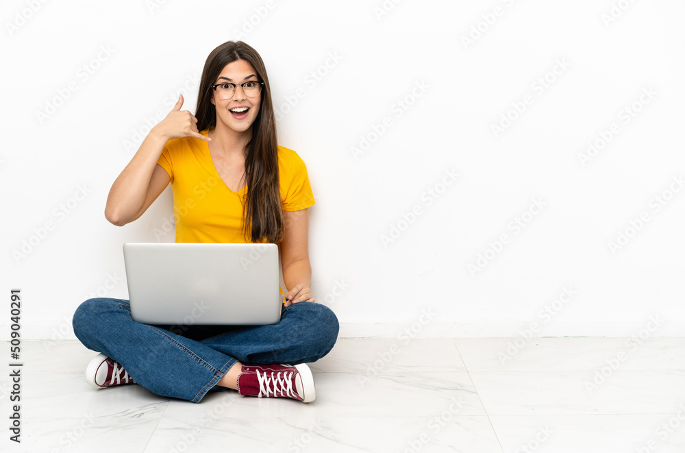 Young woman with a laptop sitting on the floor making phone gesture. Call me back sign Young woman with a laptop sitting on the floor making phone gesture. Call me back sign