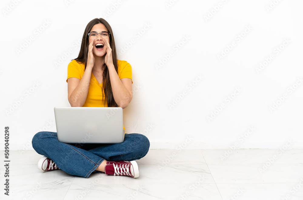 Young woman with a laptop sitting on the floor shouting and announcing something Young woman with a laptop sitting on the floor shouting and announcing something