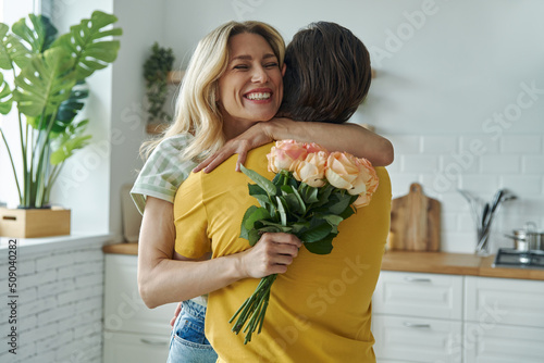 Φωτογραφία Young man surprises his girlfriend with bunch of flowers at the kitchen