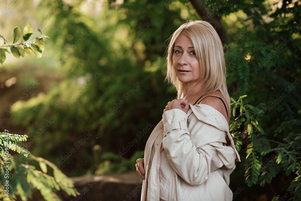 A beautiful adult woman with blond hair and a light raincoat smiles A beautiful adult woman with blond hair and a light raincoat smiles