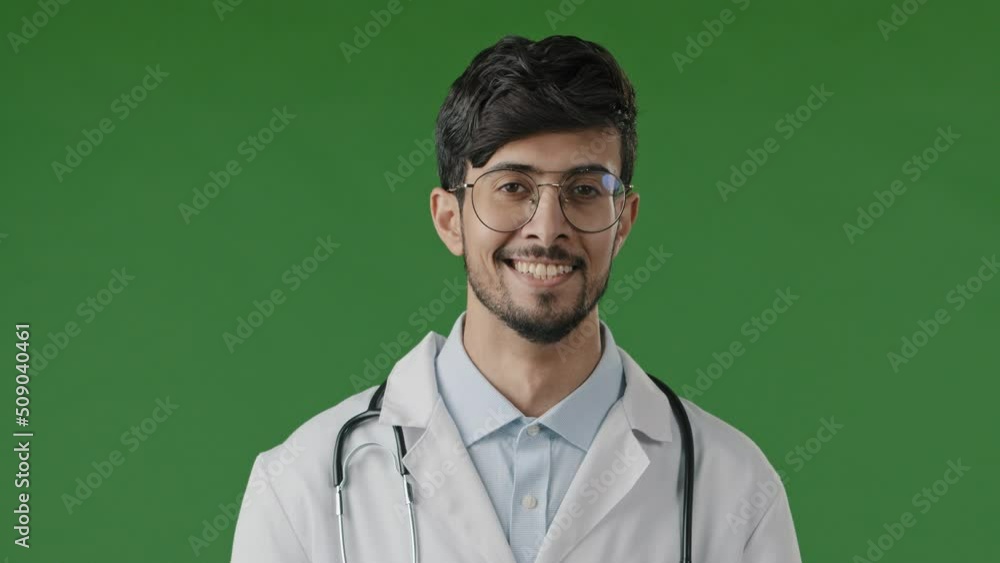 Portrait of smiling arab guy pharmacist therapist professional physician doctor wears white coat with stethoscope look at camera male medical adviser stand posing isolated in green studio background Portrait of smiling arab guy pharmacist therapist professional physician doctor wears white coat with stethoscope look at camera male medical adviser stand posing isolated in green studio background
