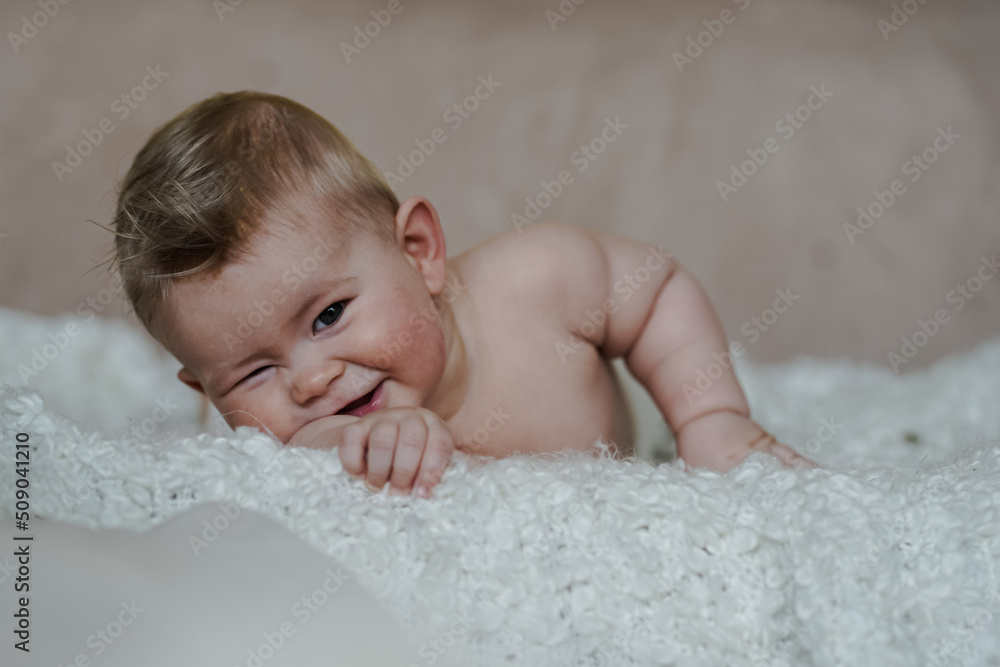 adorable naked 6 month old baby boy lying on belly and looking up in prone position after bathing wrapped in white towel at home on the couch in the living room adorable naked 6 month old baby boy lying on belly and looking up in prone position after bathing wrapped in white towel at home on the couch in the living room