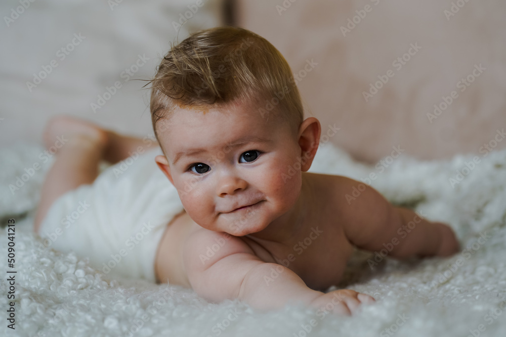adorable naked 6 month old baby boy lying on belly and looking up in prone position after bathing wrapped in white towel at home on the couch in the living room adorable naked 6 month old baby boy lying on belly and looking up in prone position after bathing wrapped in white towel at home on the couch in the living room