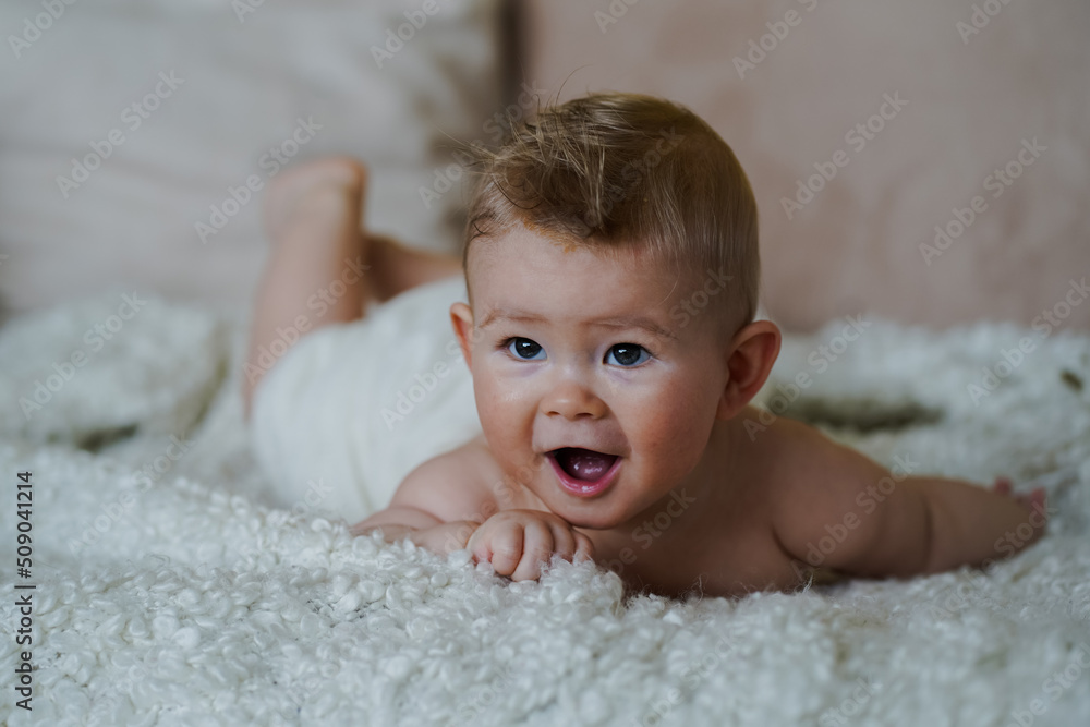 adorable naked 6 month old baby boy lying on belly and looking up in prone position after bathing wrapped in white towel at home on the couch in the living room adorable naked 6 month old baby boy lying on belly and looking up in prone position after bathing wrapped in white towel at home on the couch in the living room