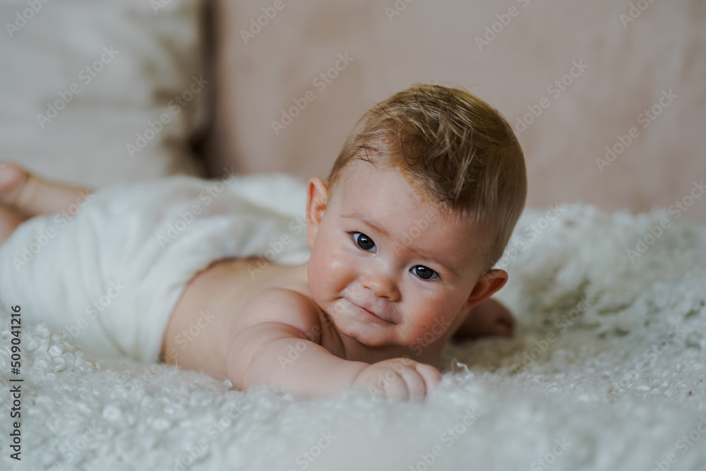 adorable naked 6 month old baby boy lying on belly and looking up in prone position after bathing wrapped in white towel at home on the couch in the living room adorable naked 6 month old baby boy lying on belly and looking up in prone position after bathing wrapped in white towel at home on the couch in the living room