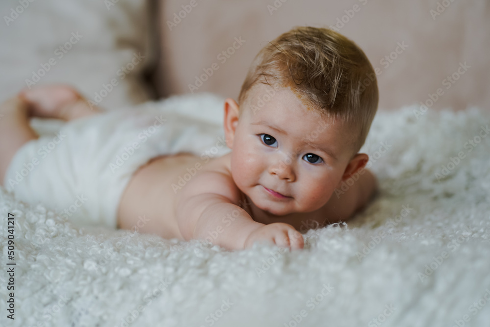 adorable naked 6 month old baby boy lying on belly and looking up in prone position after bathing wrapped in white towel at home on the couch in the living room adorable naked 6 month old baby boy lying on belly and looking up in prone position after bathing wrapped in white towel at home on the couch in the living room