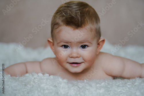  adorable naked 6 month old baby boy lying on belly and looking up in prone position after bathing wrapped in white towel at home on the couch in the living room