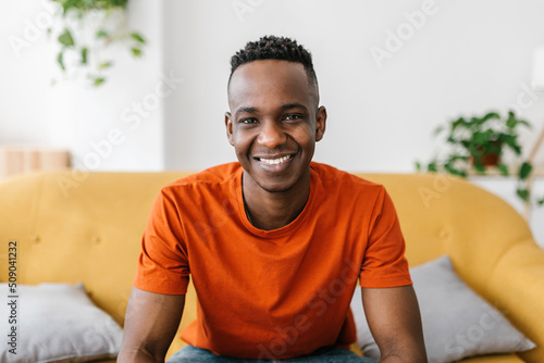 Confident young adult african man smiling at camera sitting on sofa at home - Happy people concept
