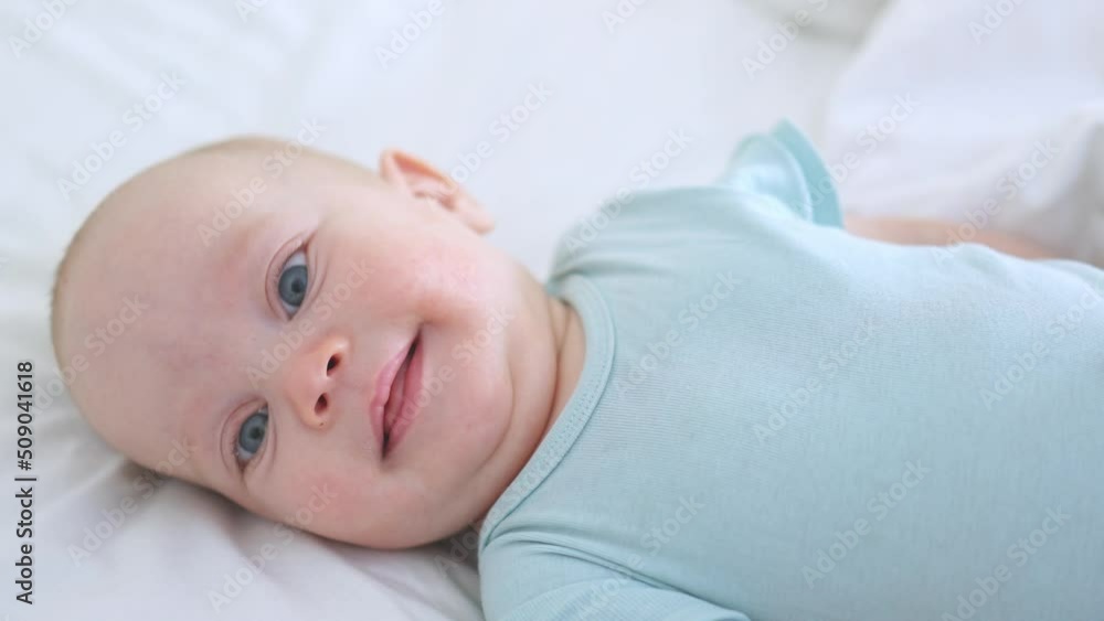 beautiful blue eyed infant baby portrait close-up, smiling face of little child lying in white bed on stomach. happy caucasian toddler baby portrait, funny kid looking camera opening mouth, emotions beautiful blue eyed infant baby portrait close-up, smiling face of little child lying in white bed on stomach. happy caucasian toddler baby portrait, funny kid looking camera opening mouth, emotions