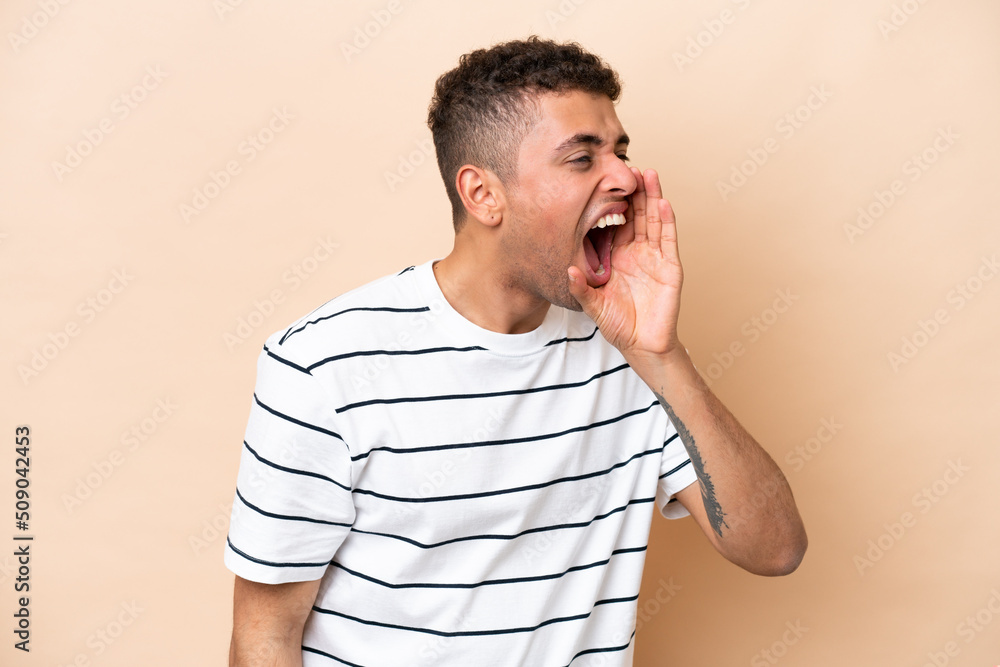 Young Brazilian man isolated on beige background shouting with mouth wide open to the side Young Brazilian man isolated on beige background shouting with mouth wide open to the side