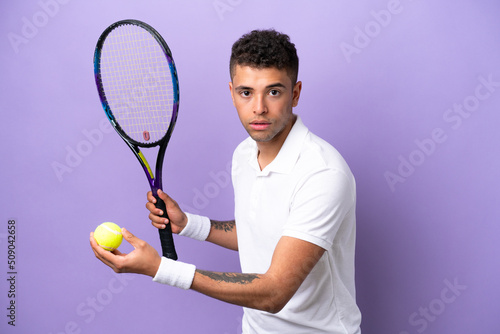 Young Brazilian man isolated on purple background playing tennis © luismolinero
