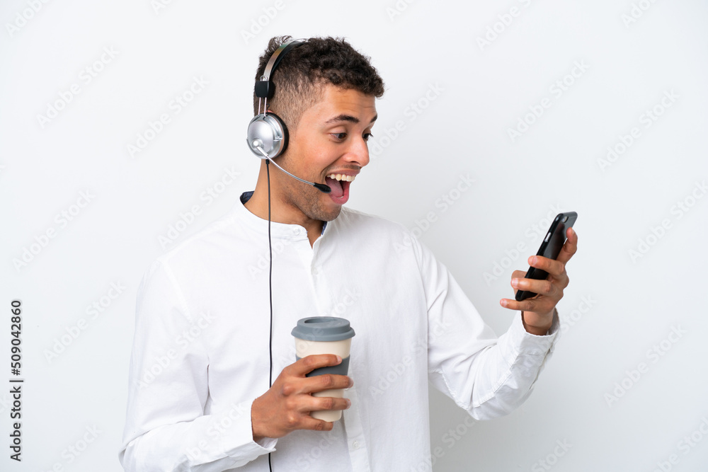 Telemarketer Brazilian man working with a headset isolated on white background holding coffee to take away and a mobile Telemarketer Brazilian man working with a headset isolated on white background holding coffee to take away and a mobile