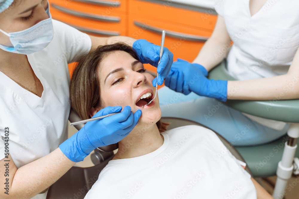 Medical treatment at the dentist office. Female dentist and assistant in dental office examining young woman with tools in dental clinic Medical treatment at the dentist office. Female dentist and assistant in dental office examining young woman with tools in dental clinic