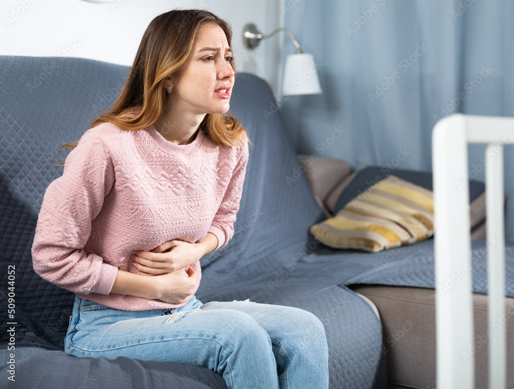 Woman sitting on couch at home and feeling stomach pain.