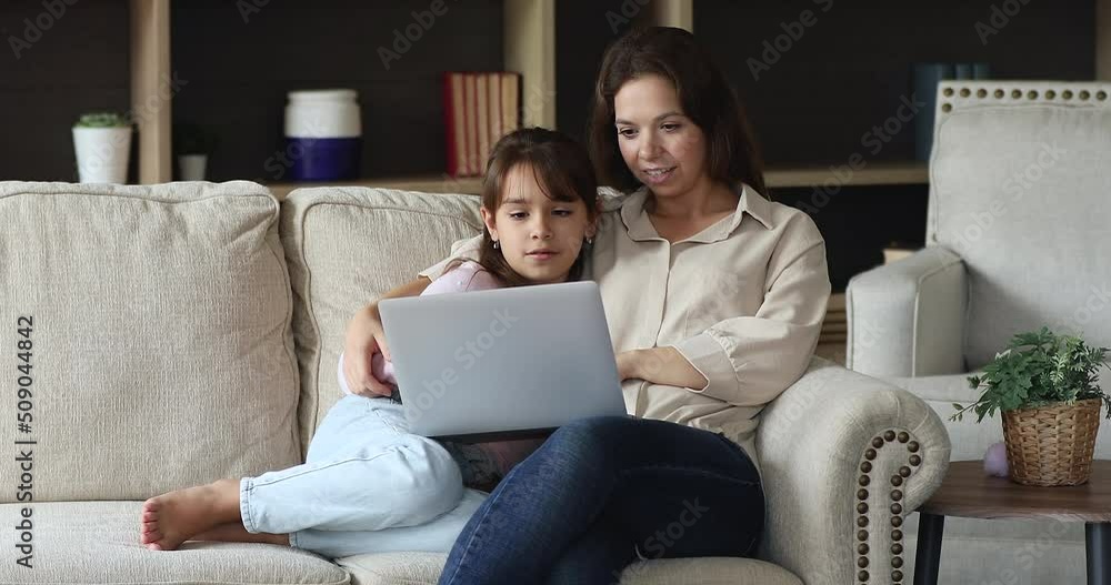 Little girl her mom watch educational on-line video, discuss purchase use retail services, do electronic shopping together at home with laptop and internet connection. E-commerce clients, fun concept Little girl her mom watch educational on-line video, discuss purchase use retail services, do electronic shopping together at home with laptop and internet connection. E-commerce clients, fun concept