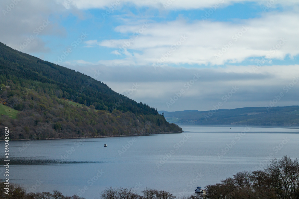 Scenic landscape view of Loch Ness in Scotland with the Scottish highlands and blue sky background, and brush vegetation in the foreground Scenic landscape view of Loch Ness in Scotland with the Scottish highlands and blue sky background, and brush vegetation in the foreground
