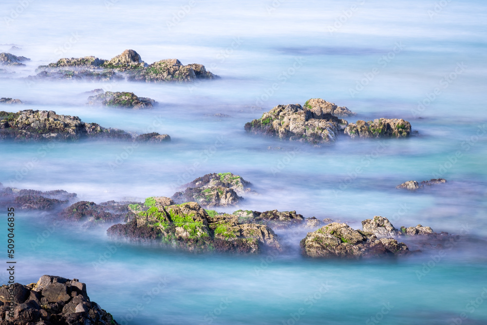 Obraz premium Serene seascape with long-exposure blue ocean water and moss-covered coastal rocks