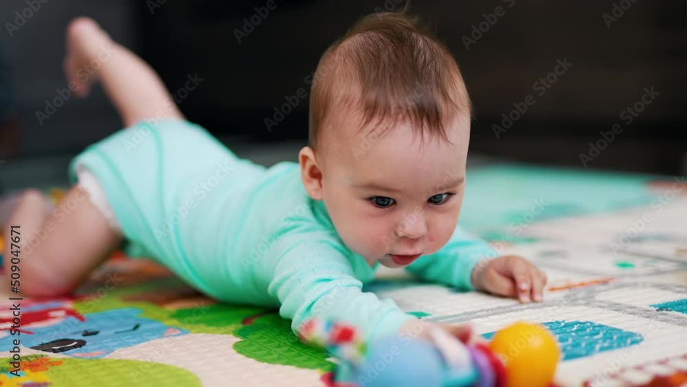 Sweetest child in blue outfit tries to reach his toy. Funny toddler takes a toy and shakes it. Blurred background. Sweetest child in blue outfit tries to reach his toy. Funny toddler takes a toy and shakes it. Blurred background.