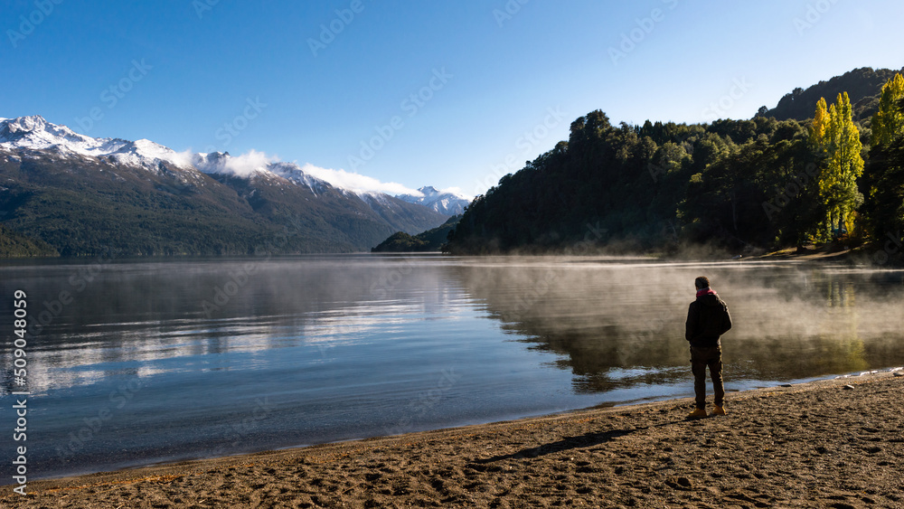 Man standing on the shores of an evaporating lake with a snowy mountain range in the background. Rivadavia Lake, Los Alerces National Park