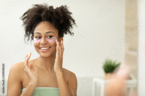 A woman applies patches under her eyes, taking care of her facial skin, standing near the mirror in the bathroom 