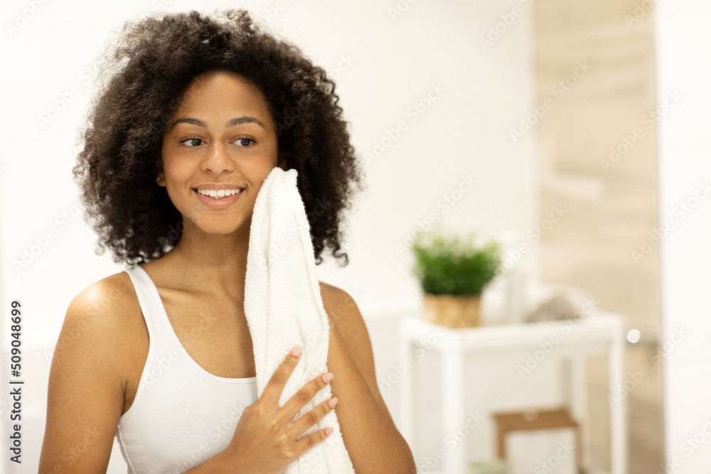 Young black woman wiping her face with a towel in the bathroom