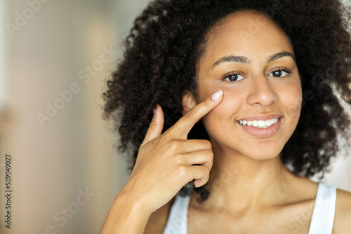 Smiling african american woman applying facial moisturizer while looking at camera.