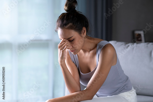Asian woman feeling sad tired and worried suffering depression in mental health, Unhappy female sitting on couch at home, thinking about problems.