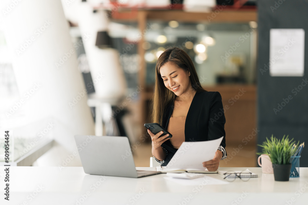Fototapeta premium Asian woman using smart phone and laptop in modern office.