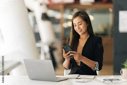 Asian woman using smart phone and laptop in modern office.