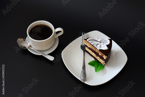 A piece of chocolate biscuit cake decorative with mint leaves and a cup of coffee on a black background.