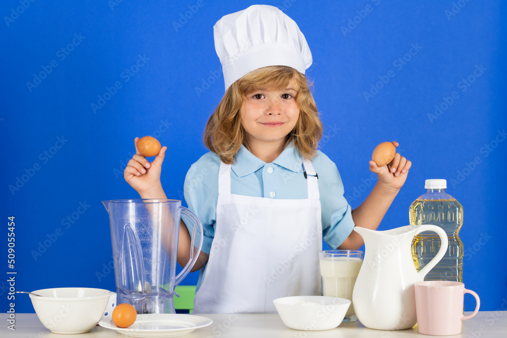 Child hold eggs wearing cooker uniform and chef hat preparing vegetables on kitchen, studio portrait. Cooking, culinary and kids food concept. Child hold eggs wearing cooker uniform and chef hat preparing vegetables on kitchen, studio portrait. Cooking, culinary and kids food concept.
