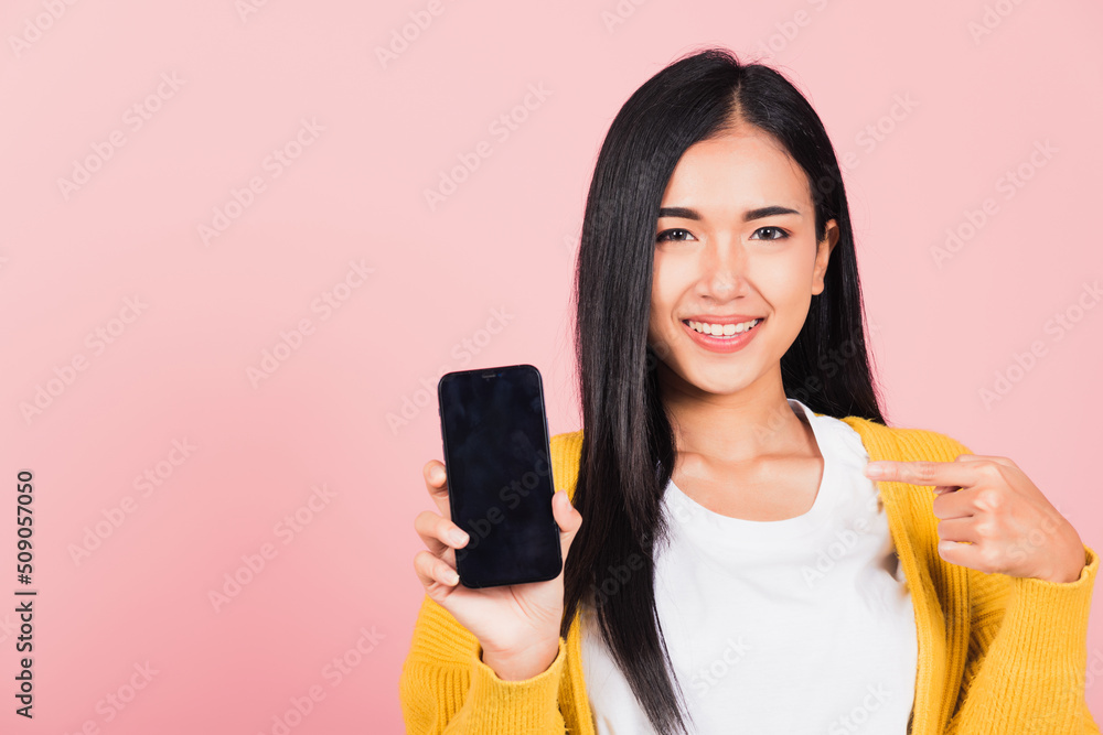 Portrait Asian happy beautiful young woman smile making finger pointing on smartphone in hand shopping online application looking to camera isolated, studio shot pink background with copy space Portrait Asian happy beautiful young woman smile making finger pointing on smartphone in hand shopping online application looking to camera isolated, studio shot pink background with copy space