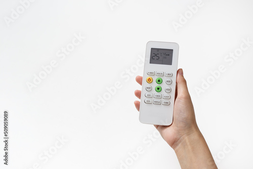 Woman's hand holding remote control of air condition that has been adjusted to 25 degrees Celsius over white background.