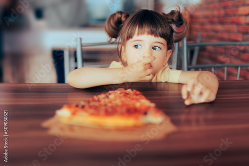 Little Toddler Girl Eating a Slice of Pizza in a Restaurant 