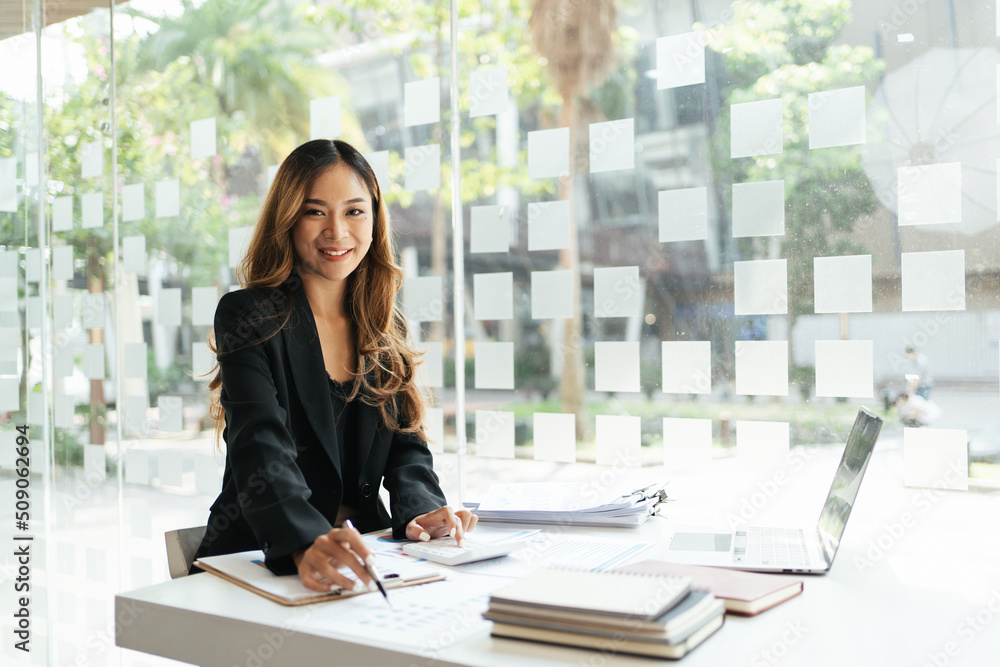 Businesswoman working on new project with laptop computer in modern office. Pretty business woman smiles at the camera while sitting at her desk in front of the computer.