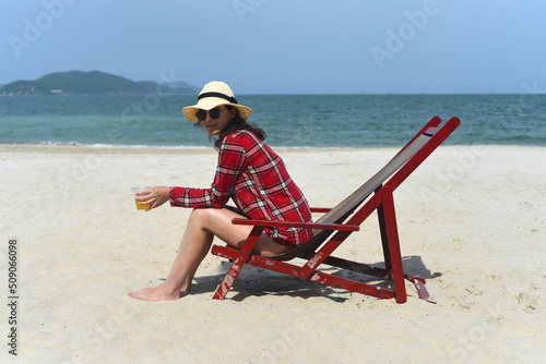 Young woman in hat sitting on the desk chair at the beach with white sand in Vietnam